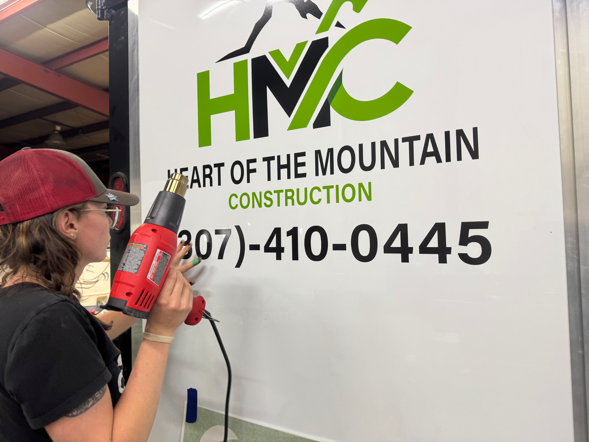 Installer heat-setting HMC Construction vinyl decal on trailer